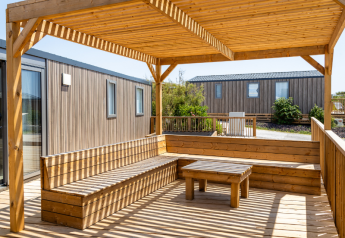 Wooden terrace seating and table at TRIBU mobile homes, Campsite Les Tamaris, France, under a pergola.