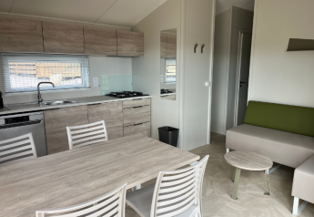 Modern TRIBU mobile home kitchen and living area at Campsite Les Tamaris in France with table and sofa.