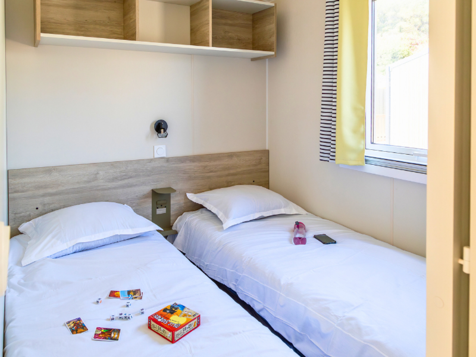 Twee eenpersoonsbedden in een lichte, moderne kamer van het Premium mobile home op Camping Les Tamaris, Frankrijk.