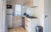 Modern kitchenette in a Premium mobile home at Campsite Les Tamaris, France, with stove and fridge.