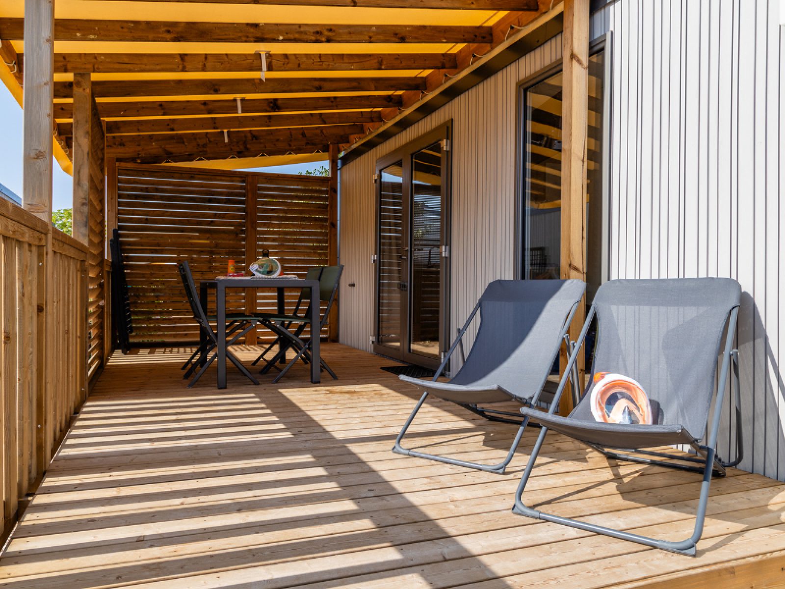 Zonnig terras met loungestoelen en eettafel bij Premium stacaravan, Camping Les Tamaris, Frankrijk.