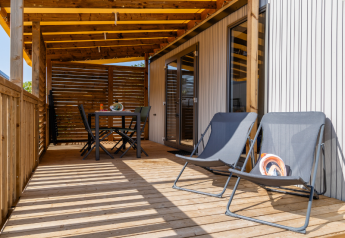 Sunny deck with lounge chairs and dining table at Premium mobile home, Campsite Les Tamaris, France.