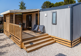 Casa móvil premium con terraza de madera, tumbonas y muebles de jardín, rodeada de grava y árboles