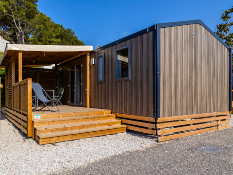 Premium mobile home at Campsite Les Tamaris in France featuring a wooden terrace and outdoor chairs.