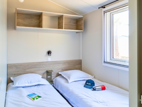 Bedroom in a Premium mobile home at Campsite Les Tamaris, France, featuring twin beds and a window.