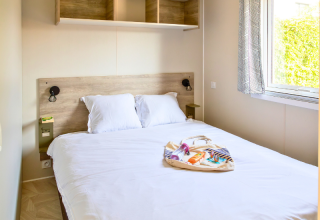 Premium mobile home bedroom with double bed, window, and bag set at Campsite Les Tamaris in France.
