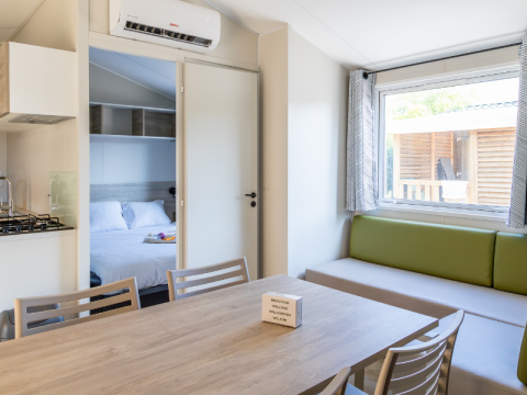 Interior of a Premium mobile home at Campsite Les Tamaris in France, showing dining area and bedroom.