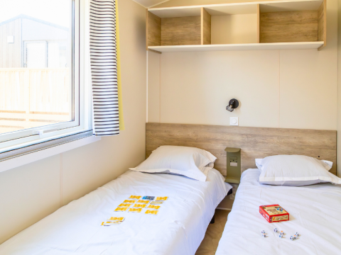 Zweibettzimmer im Premium Mobile Home auf dem Campingplatz Les Tamaris in Frankreich, mit Fenster und Ablage.