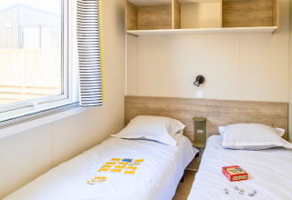 Twin bedroom in Premium Mobile Home at Campsite Les Tamaris, France, featuring beds, window, and shelves.