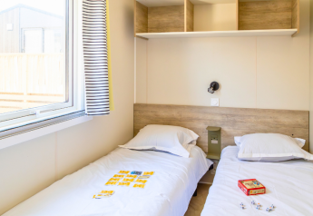 Twin bedroom in Premium Mobile Home at Campsite Les Tamaris, France, featuring beds, window, and shelves.