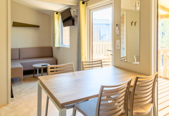 Vista interior de la Premium Mobile Home en el Camping Les Tamaris en Francia con mesa y sofá.