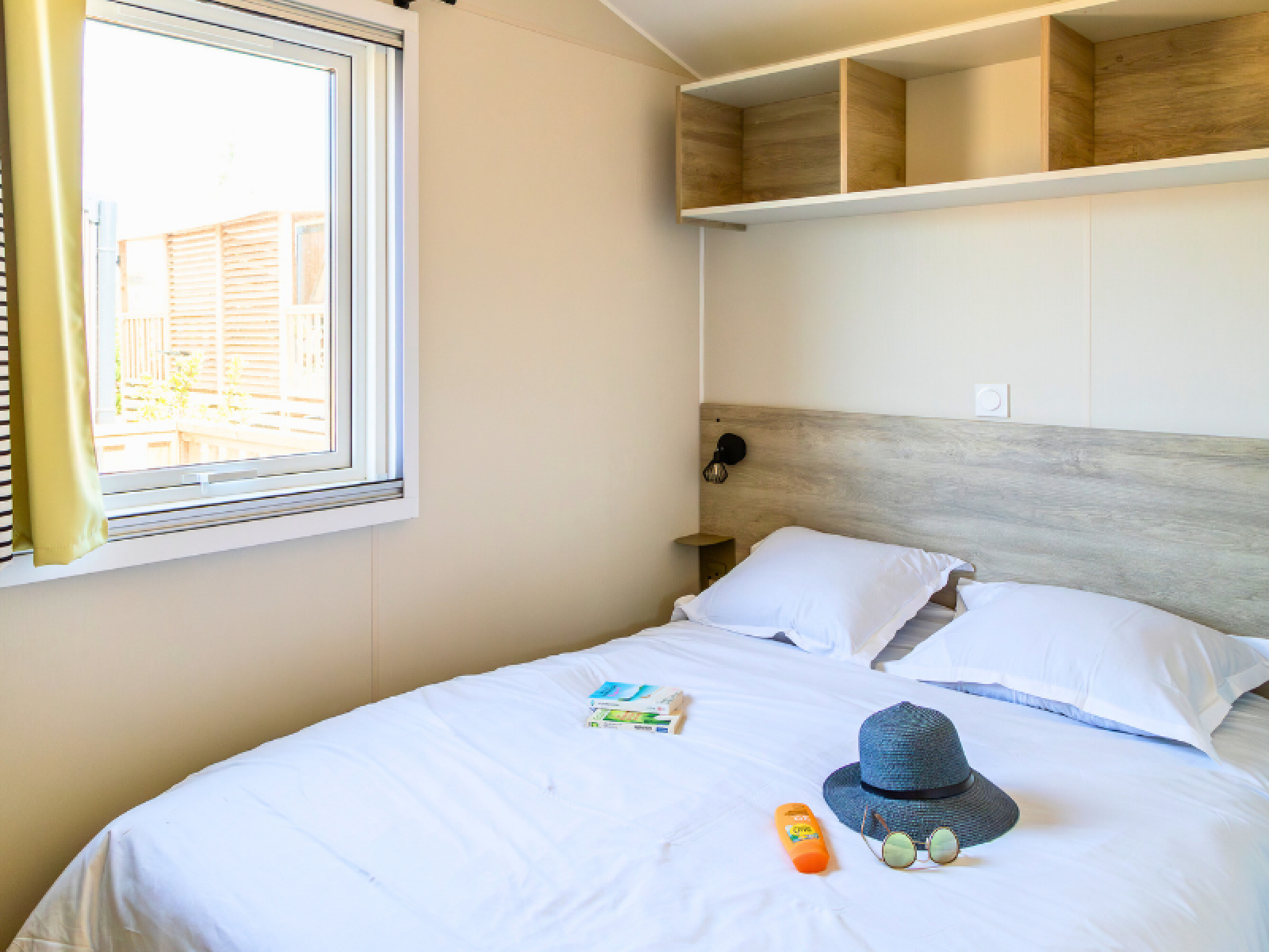 Slaapkamer in Premium Mobile Home op Camping Les Tamaris, Frankrijk, met tweepersoonsbed en zonnehoed.