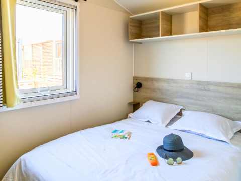 Camera da letto nel Premium Mobile Home al Campeggio Les Tamaris in Francia con letto matrimoniale e oggetti estivi.