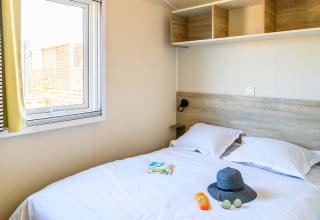 Slaapkamer in een Premium Mobile Home op Camping Les Tamaris, Frankrijk, met dubbel bed en reisbenodigdheden.