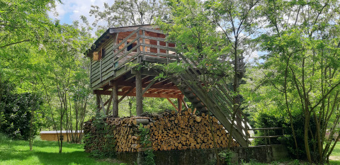 Treehouse-style wooden cabin on stilts with stacked firewood underneath at Ushuaïa Villages Le Viaduc campsite.