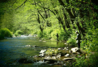 Two people fly fishing by a scenic forest river near Arlebosc in the Auvergne-Rhône-Alpes region of France.