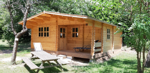 Una baita in legno al campeggio Ushuaïa Villages Le Viaduc, circondata da alberi e tavolo da picnic davanti.