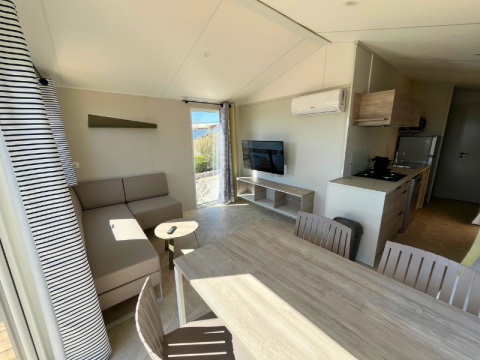 Soggiorno della Premium Mobile Home «Large» al campeggio Les Tamaris in Francia con divano e cucina.