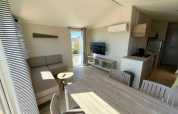 Living room in Premium Mobile Home «Large» at Campsite Les Tamaris, France, featuring sofa and kitchen.