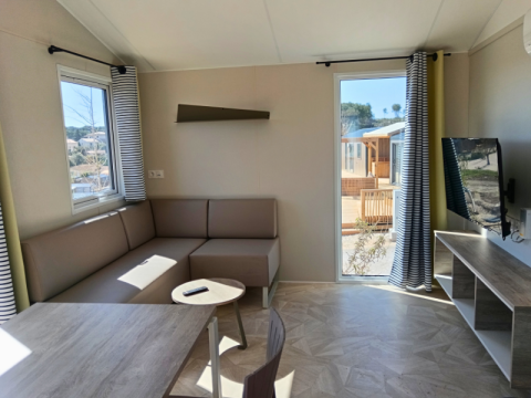 Soggiorno moderno della Premium Mobile Home «Large» al Campeggio Les Tamaris con divano e TV.
