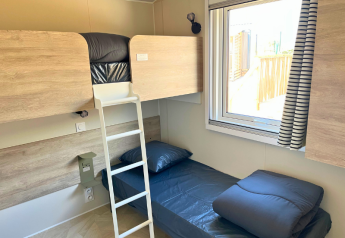 Room with bunk bed and single bed in Premium Mobile Home 'Large' at Campsite Les Tamaris, France.