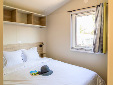 Camera da letto nel Premium Mobile Home «Large» al campeggio Les Tamaris, Francia, con letto e finestra.