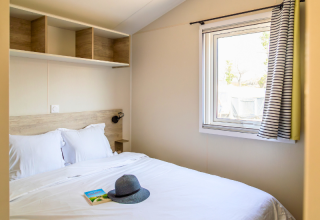 Camera da letto nel Premium Mobile Home «Large» al campeggio Les Tamaris, Francia, con letto e finestra.