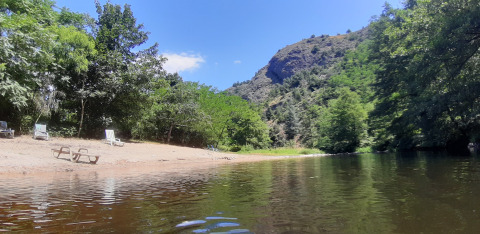 Spiaggia fluviale con lettini e alberi al campeggio Ushuaïa Villages Le Viaduc in Auvergne-Rhône-Alpes, Francia.