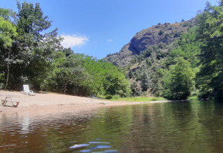 Spiaggia fluviale con lettini e alberi al campeggio Ushuaïa Villages Le Viaduc in Auvergne-Rhône-Alpes, Francia.