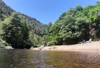 Tranquil riverbank with lounge chairs at Campsite Ushuaïa Villages Le Viaduc, Auvergne-Rhône-Alpes, France.