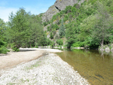 Riverbank with greenery and hillside views at Ushuaïa Villages Le Viaduc campsite in south-central France.