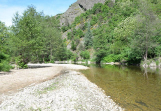 Riva di fiume con vegetazione lussureggiante al campeggio Ushuaïa Villages Le Viaduc in Francia.