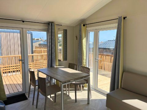 Interno della Premium Mobile Home «Large» con tavolo da pranzo, sedie e accesso alla terrazza a Les Tamaris.