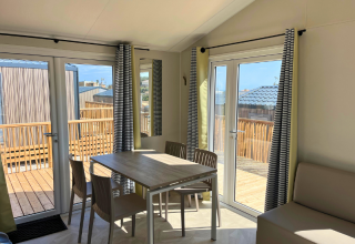 Interno della Premium Mobile Home «Large» con tavolo da pranzo, sedie e accesso alla terrazza a Les Tamaris.