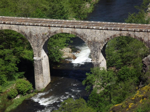 Stone bridge crossing a river surrounded by lush green trees near Arlebosc, Auvergne-Rhône-Alpes, France.