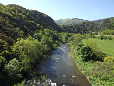 Fiume che scorre in una valle verde presso Ushuaïa Villages Le Viaduc, Auvergne-Rhône-Alpes, Francia, tra le colline.