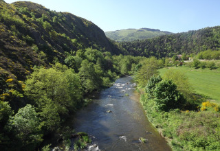 River flowing through lush valley at Campsite Ushuaïa Villages Le Viaduc, Auvergne-Rhône-Alpes, France, with hills.