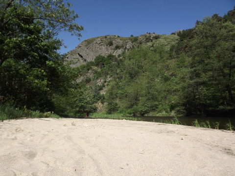 Spiaggia sabbiosa al campeggio Ushuaïa Villages Le Viaduc, circondata da alberi e colline in Francia.