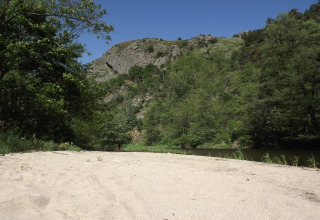 Spiaggia sabbiosa al campeggio Ushuaïa Villages Le Viaduc, circondata da alberi e colline in Francia.