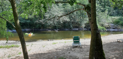 Peaceful riverside beach with a green chair, trees, and a person canoeing, Ushuaïa Villages Le Viaduc, France.