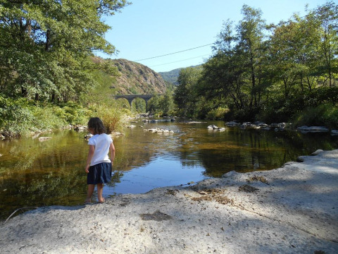 Un bambino in riva a un fiume limpido vicino Ushuaïa Villages Le Viaduc con un viadotto tra le colline.