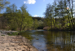 Tranquil river with sandy shore and green trees at Ushuaïa Villages Le Viaduc campsite, Auvergne-Rhône-Alpes, France.