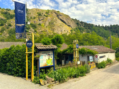 Entrance of Ushuaïa Villages Le Viaduc campsite in Auvergne-Rhône-Alpes, France, surrounded by lush hills.