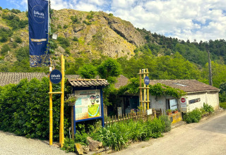 Entrance of Ushuaïa Villages Le Viaduc campsite in Auvergne-Rhône-Alpes, France, surrounded by lush hills.