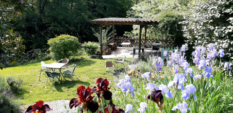 Giardino fiorito con pergolato e tavoli all’aperto nel campeggio Ushuaïa Villages Le Viaduc, Francia.