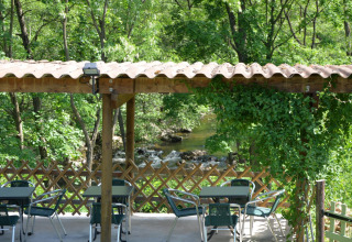 Terrazza all'aperto con tavoli e sedie al Campeggio Ushuaïa Villages Le Viaduc immersa nel verde.