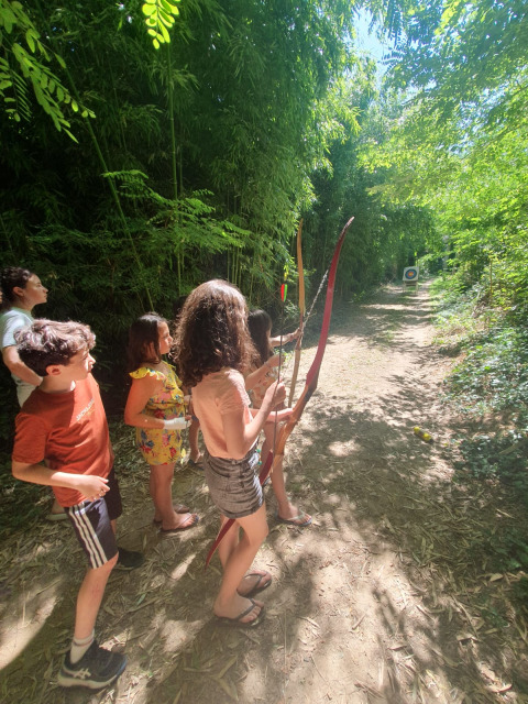 Bambini si divertono con il tiro con l’arco nella radura del campeggio Ushuaïa Villages Le Viaduc, Francia.