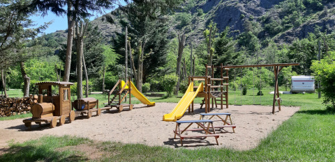 Parco giochi con scivoli, altalene e trenino di legno al campeggio Ushuaïa Villages Le Viaduc, Francia.