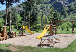 Playground with slides, swings and wooden train at Ushuaïa Villages Le Viaduc campsite in France.