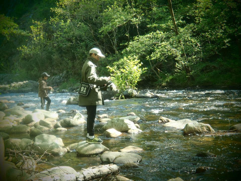 Due persone pescano in un fiume roccioso circondato dalla foresta al campeggio Ushuaïa Villages Le Viaduc in Francia.